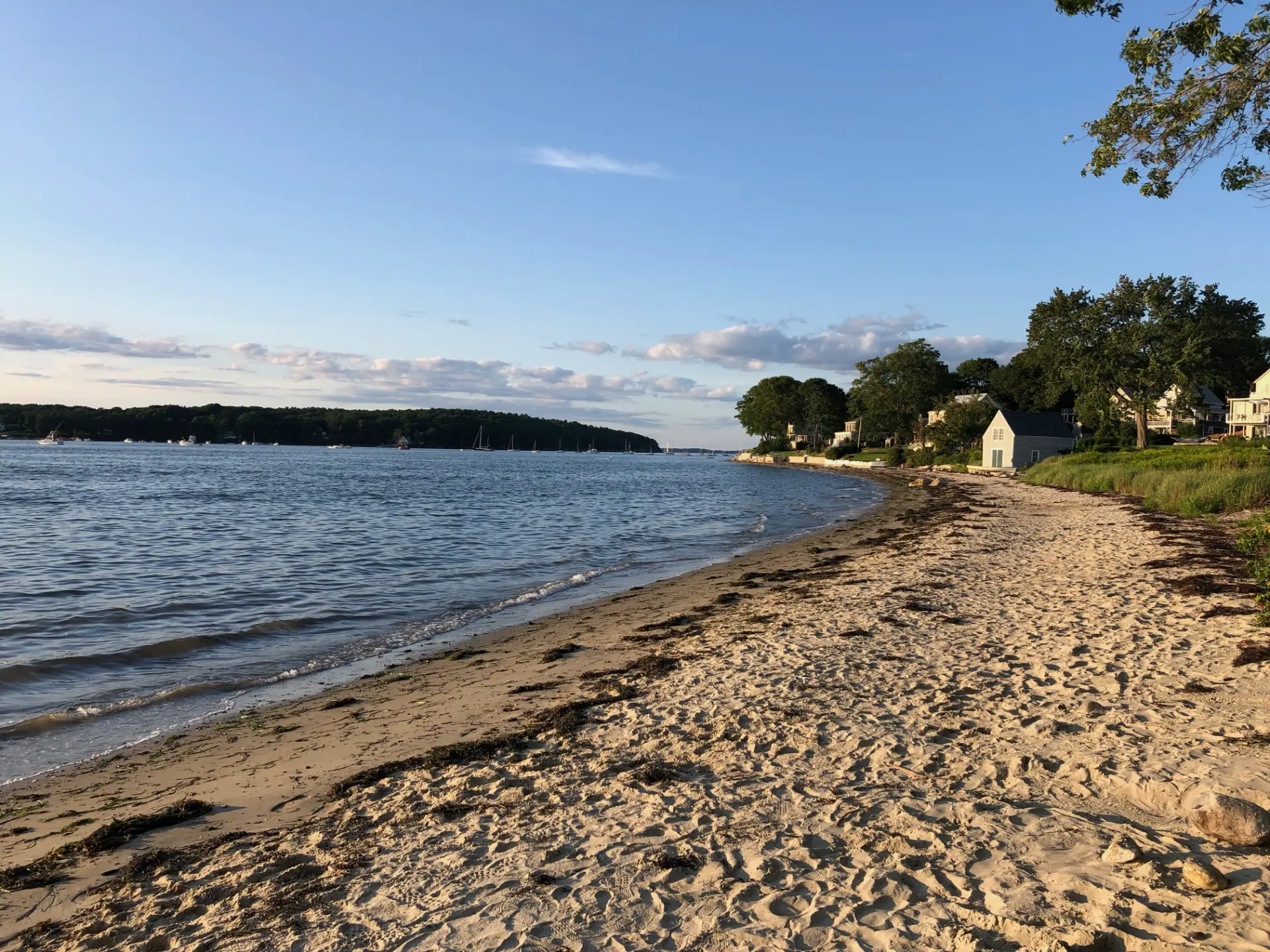 Wide sandy stretch of Centennial Beach on Peaks Island with moored sailboats offshore