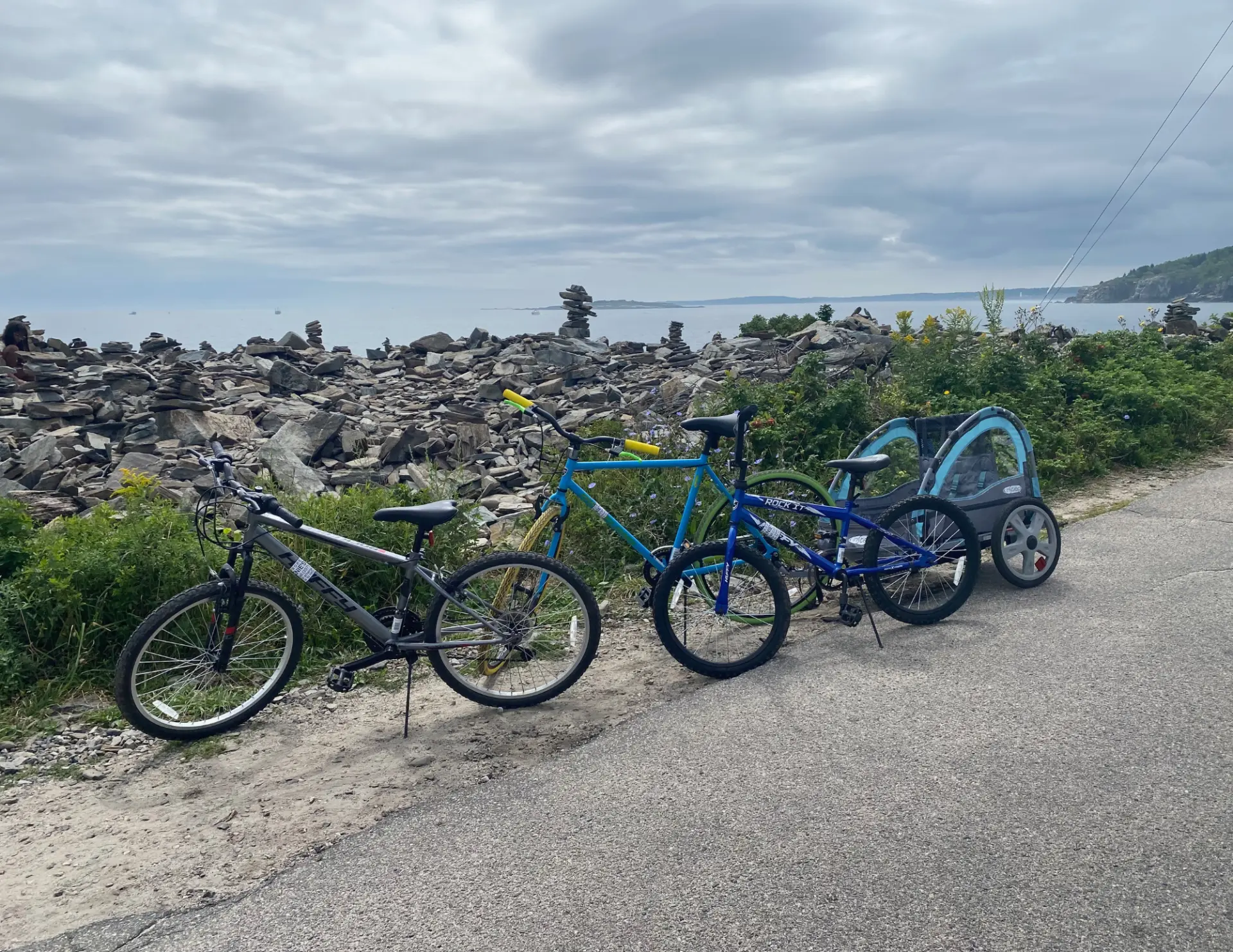 Rental bikes and kid trailer parked along the rocky Peaks Island back shore